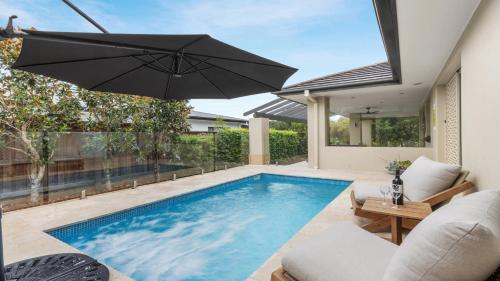a swimming pool with an umbrella next to a house at La Vita - The Vintage in Pokolbin