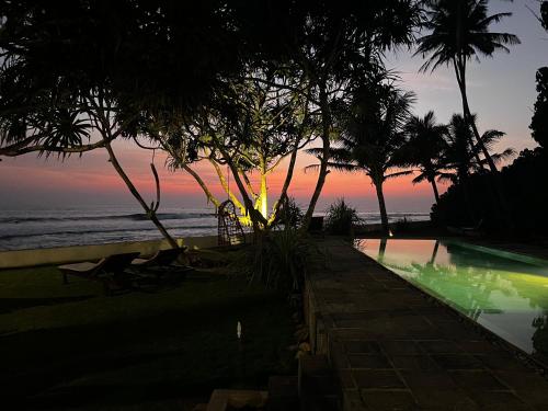 a swimming pool with trees and the ocean at sunset at Saltasia Boutique Beach Villa in Mirissa