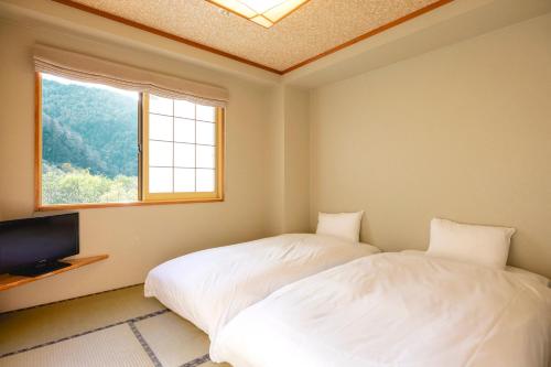 two beds in a room with a window and a television at Shikishimaso in Higashikawa