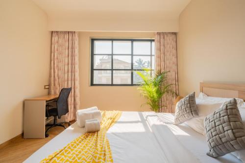 a bedroom with a bed with a desk and a window at ELIVAAS Kamerios Maris 1BHK Apartment with Jacuzzi in Goa