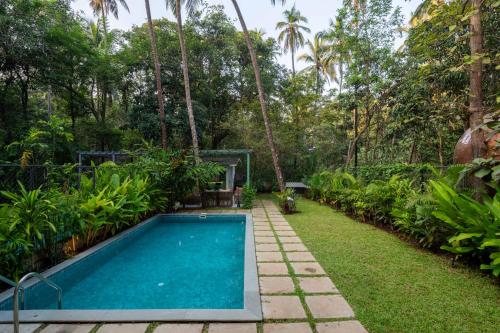 a swimming pool in a garden with palm trees at Verona by Vianaar Luxe Garden Pool Villa Assagao in Goa