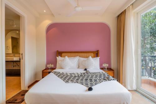 a bedroom with a white bed with a pink wall at ELIVAAS Solace Azure 4 BHK Villa with Pvt Pool in Calangute