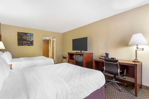a hotel room with two beds and a desk and a tv at Clarion Pointe Research Triangle Park Durham in Durham