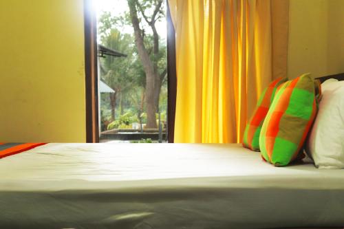 a bedroom with a bed with colorful pillows and a window at Leon Lakeside Hotel - Kataragama in Gotamegama