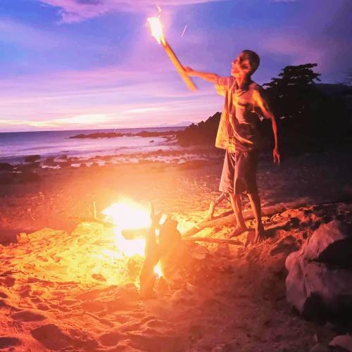 a boy standing on the beach with a fire on the beach at DD Beach Houses in Phra Ae beach
