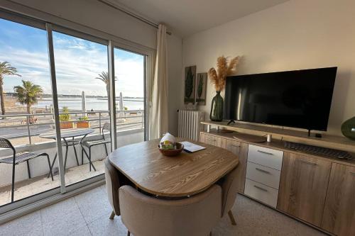d'un salon avec une table et une télévision ainsi que d'un balcon. dans l'établissement L'Impérial 1- Appartement tout confort 1 chambre Vue mer, au Grau-du-Roi