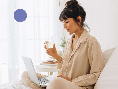 a woman sitting on a couch with a laptop and a wine glass at Hotel UND - smart alpine stay in Schladming