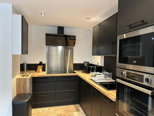 une cuisine avec des armoires noires et des appareils en acier inoxydable dans l'établissement Odalys Chalet L'Arpette Lodge, à La Plagne Tarentaise