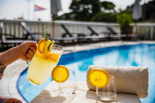a person holding a glass of orange juice next to a pool at Amadria Park Grand Hotel 4 Opatijska Cvijeta in Opatija