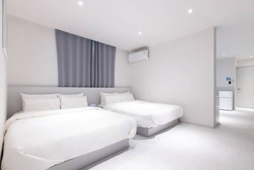 a white bedroom with two beds and a window at 은행 아늑에어 대전역점 Aank Air Hotel Daejeon Station in Daejeon