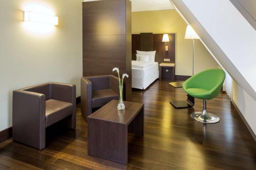 a hotel room with a bed and a green chair at NH Collection Dresden Altmarkt in Dresden