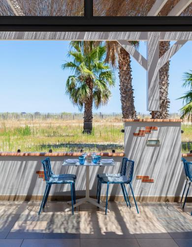a patio with a table and chairs and palm trees at Les Bulles de Mer - Hotel & Spa sur la Plage in Saint-Cyprien