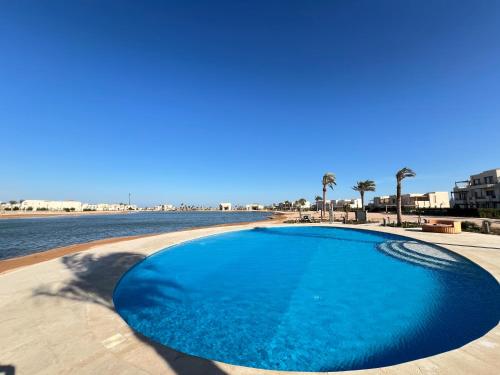 a large blue swimming pool next to a body of water at Stylish 1BR Ground With Free Pool & Lagoon Access In Gouna in Hurghada