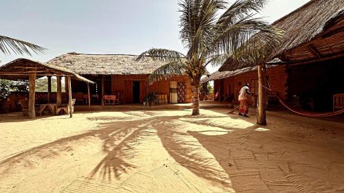 a man standing in front of a building with a palm tree at Nguel du Saloum - Chez Abdou et Mar in Mar Lodj