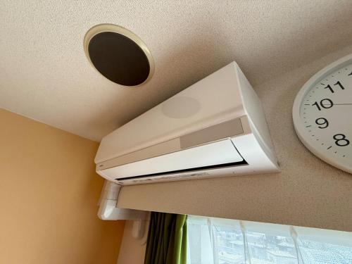 a white air conditioner on a ceiling next to a clock at 8-1閑静なエリア豊平川目の前でゆったりと静かな旅行可能 in Sapporo