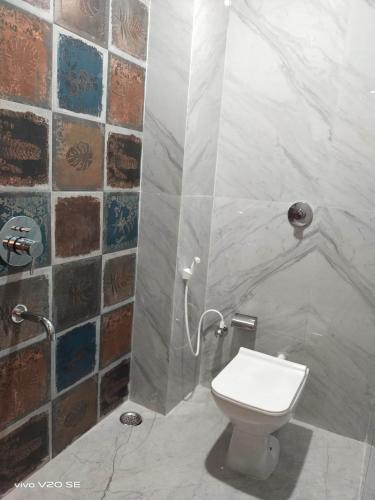 a bathroom with a toilet and a tiled wall at Maa Paradise World in Alīpur Duār