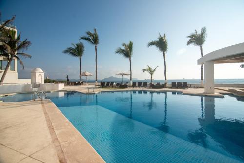 a swimming pool with palm trees and the ocean at Vista al Mar, Terraza y Albercas in Manzanillo
