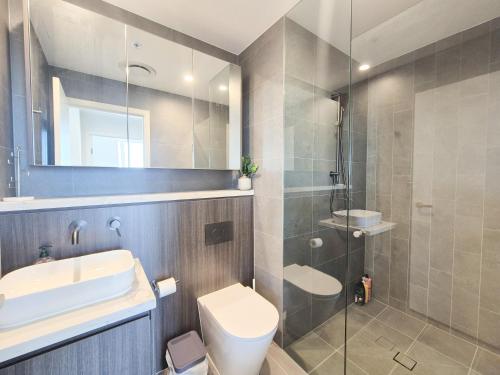 a bathroom with a toilet and a sink and a shower at Olympic Park Escape 2BR w Gym, Pool & Free Parking in Sydney