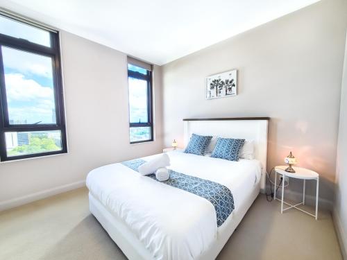 a white bedroom with a bed and two windows at Olympic Park Escape 2BR w Gym, Pool & Free Parking in Sydney