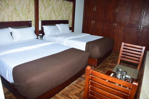 two beds in a hotel room with two chairs at Jeyam Palace by Whynter Stays in Kodaikānāl