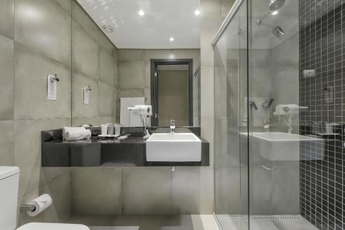 a bathroom with a sink and a glass shower at Grand Mercure Curitiba Rayon in Curitiba