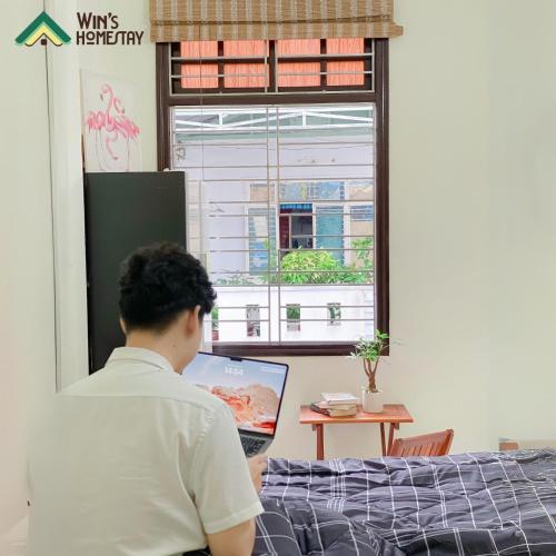 a man sitting on a bed using a laptop computer at Win's Homestay in Danang