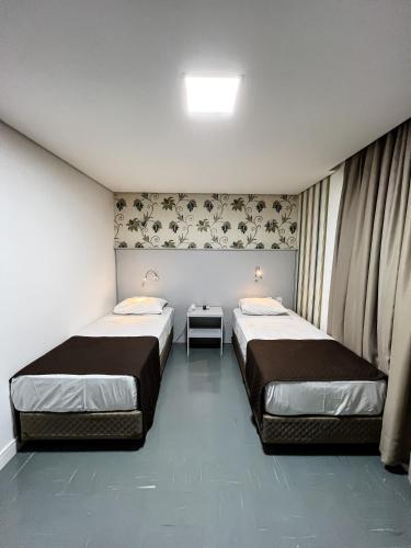two beds in a small room with two tables at Life Hotel in Canoas