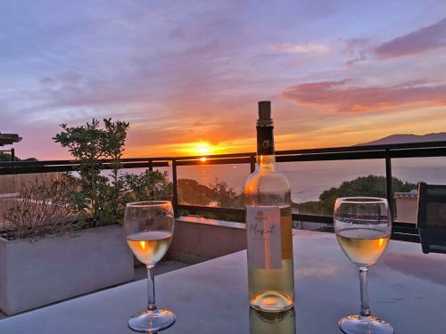 - une bouteille de vin et deux verres sur une table au coucher du soleil dans l'établissement So Leil So Fun à Porticcio - 45m2 - Grand lit 180 - Plage à pied - Wifi fibre - Terrasse, à Porticcio