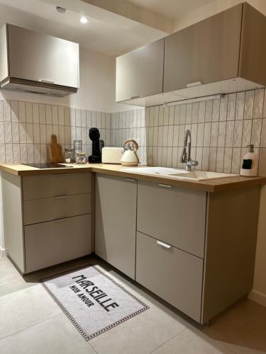 - une cuisine avec des placards blancs, un évier et un tapis dans l'établissement Le Camas Cosy - Rez de Jardin, à Marseille