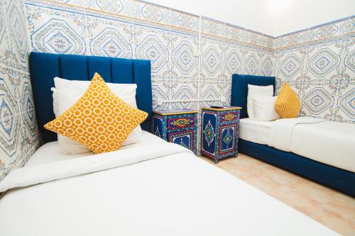 two beds in a room with blue and yellow pillows at Riad Dar Kella in Marrakech