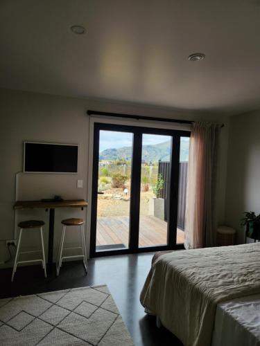 a bedroom with a bed and a desk and a sliding glass door at Escape to Riverslea in Wanaka