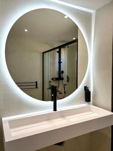 La salle de bains est pourvue d'un miroir rond et d'un lavabo. dans l'établissement Appart 'COSY avec Piscine Chauffée Privée, à Salon-de-Provence