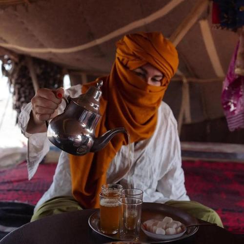a woman wearing a hijab holding a tea kettle at Merzouga Horizon Luxury Camp in Merzouga