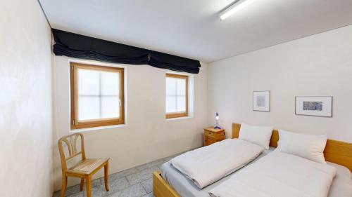 a bedroom with a bed and a chair and two windows at Chalet Rominger-Surlej in Surlej