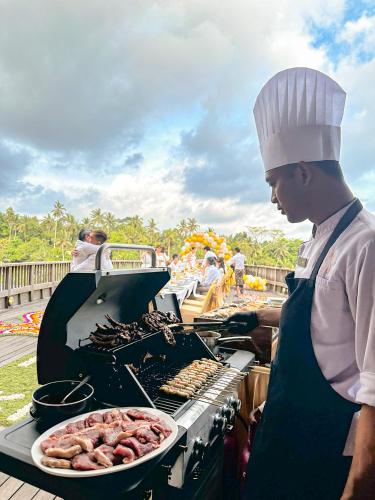 a man is cooking food on a grill at Kastara Resort in Ubud