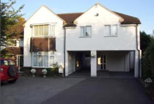 a white house with a car parked in front of it at Watts Lodge in Bicester