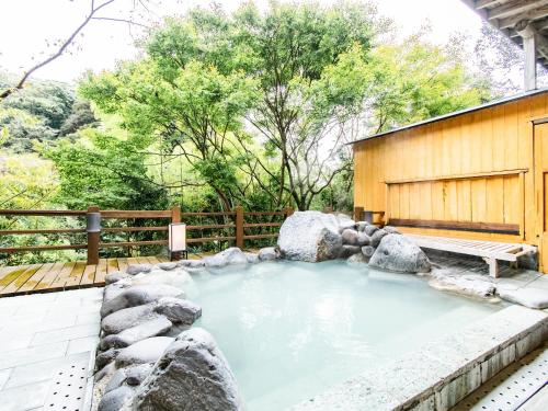 a hot tub in a backyard with rocks and a bench at Kirishima Momijidani Seiryuso in Kirishima