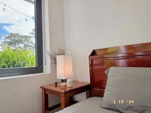 a bed with a lamp on a table next to a window at Sunflower Garden Homestay Đà Lạt in Xuan An