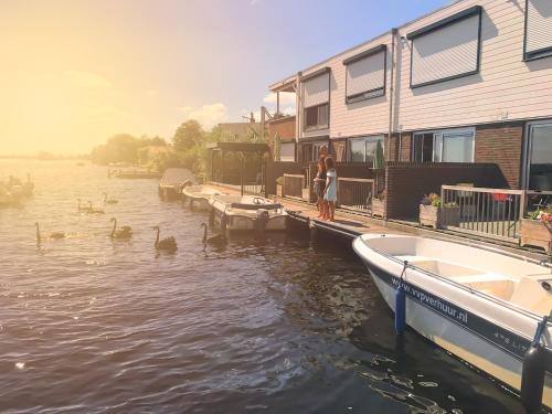 a woman standing at a dock with ducks in the water at VISSERSLUST Rooms, Apartments and Houseboats in Vinkeveen