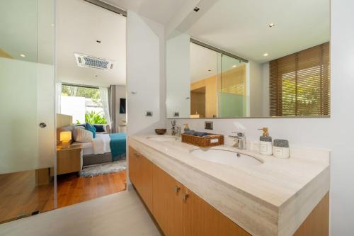 une salle de bain avec un lavabo et un grand miroir dans l'établissement Bang Tao Botanica Modern Loft 3 bd, à Ban Pak Lak
