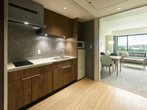 a kitchen with wooden cabinets and a dining room with a table at Mitsui Garden Hotel Kashiwa-no-ha Park Side - Chiba in Kashiwa