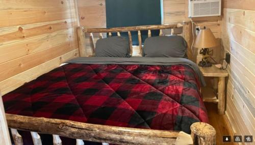 a bed in a cabin with a red and black quilt at Black Bear Cabin in Black River Falls