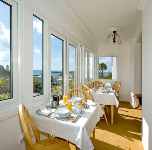 a dining room with white tables and chairs and windows at Seaview in Looe