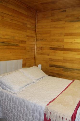 a bedroom with a white bed with wooden walls at Pousada Vila Felicita in São Valentim