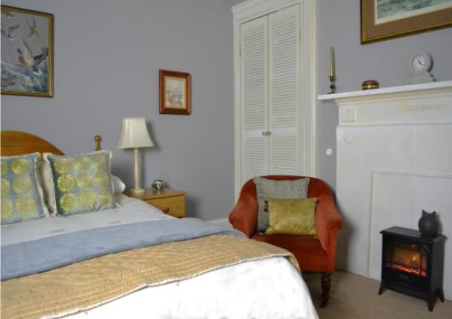 a bedroom with a bed and a chair with a fire place at Maybank Guest House in Helensburgh