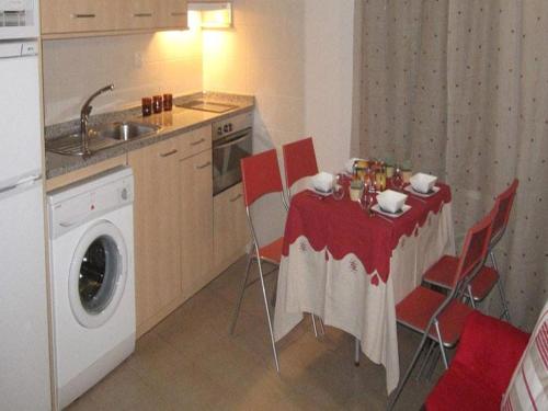 a kitchen with a table with red chairs and a washing machine at Apartamentos Casbas in Sorripas