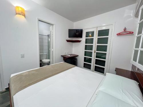 a white bedroom with a bed and a tv at Pousada Promessa Amanay antigamente Ubatuba Guest House in Ubatuba