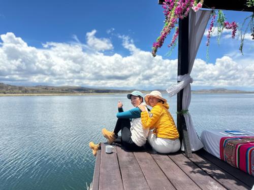 two women sitting on a dock next to the water at Uros Titicaca Beluxia in Puno