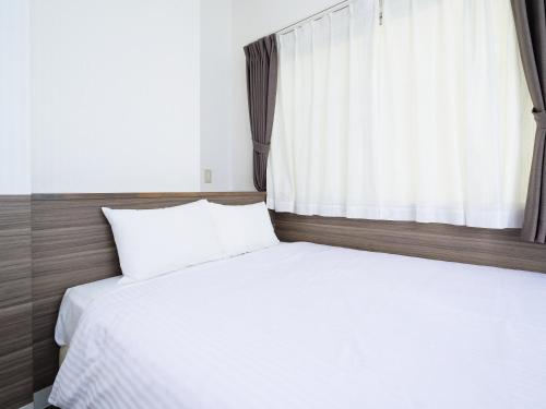 a bed with white sheets and a window at HOTEL THE CUBE Naha Kokusai Street in Naha