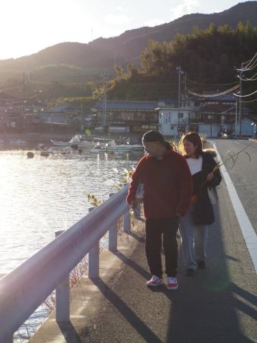 a man and a woman walking on a bridge near the water at Guesthouse SETOUCHI LIFE in Kure
